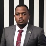 Business portrait of a black man wearing formal attire against a striped background.