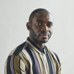 Close-up portrait of a confident man with a beard in a striped shirt, indoors.